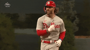 Sports gif. Bryce Harper of the Phillies in a jersey and batter's helmet running in slow motion as he yells with excitement. 