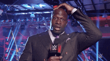 Sports gif. Titus O'neil stares at us frozen from shock. His hand rests on the top of his head and his mouth is left open like he’s paused mid action.