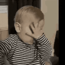 Video gif. A baby with a pacifier in his mouth, has his hand over his eyes and leans down a bit as he rubs his face looking unhappy or tired. 