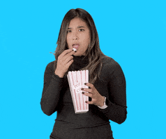 Video gif. Holding a popcorn container and tossing kernels into her mouth, a woman nods agreeably.