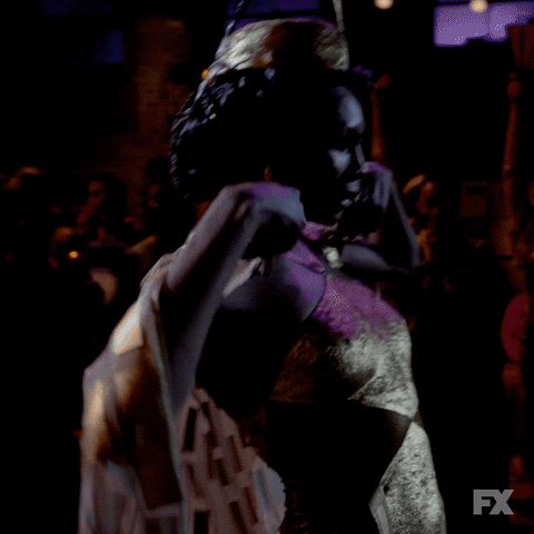 TV gif. Dominique Jackson as Elektra Abundance in Pose, drops her cape to reveal her outfit, striking an elegant pose, then, basking in the spotlight, strikes another.