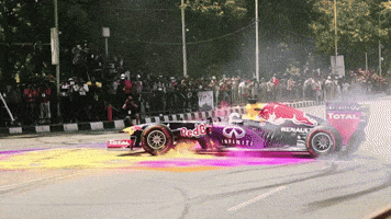 Sports gif. A race car spins around in a circle on top of pink and yellow pigments, spreading huge clouds of colorful dust in the air.