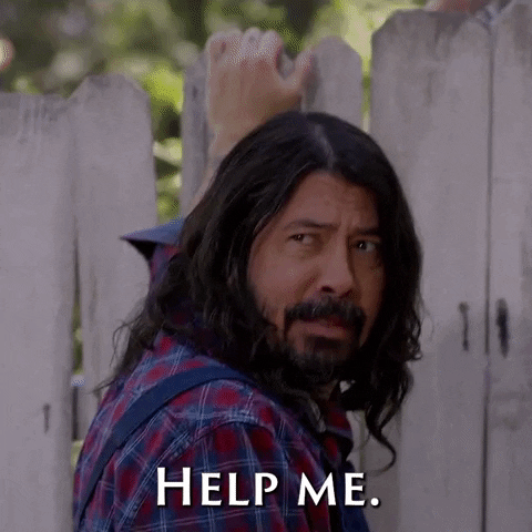Celebrity gif. Dave Grohl of the Foo Fighters leans onto an old fence and turns to speak to someone. He has a worried, pleading look on his face as he says, “help me.” 