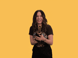 Celebrity gif. Sophia Bush pops open a bottle of champagne and yelps in glee as confetti falls around her.