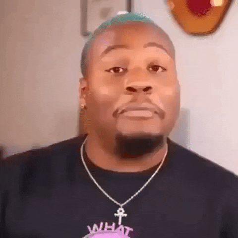 Video gif. Man wearing ankh necklace, with close-cropped turquoise hair, tries to keep a straight face and appear serious while laughing.