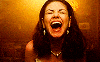 TV gif. Mila Kunis as Jackie on That '70s Show cracks up, laughing and reeling backward in a smoky room.