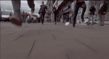 Movie gif. Ewan McGregor as Mark and Ewen Bremner as Spud in Trainspotting run away in a sprint down a busy walkway. 