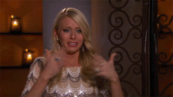 Reality TV gif. In a "confessional" segment, a blonde woman with a sequined shirt and big earrings fans her face with her hands as she begins to cry.