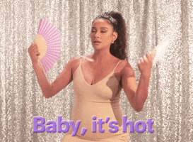 Celebrity gif. Shay Mitchell wears a low cut dress and sighs as she fans herself with two paper fans, looking up in discomfort. Text, "Baby, it's hot."