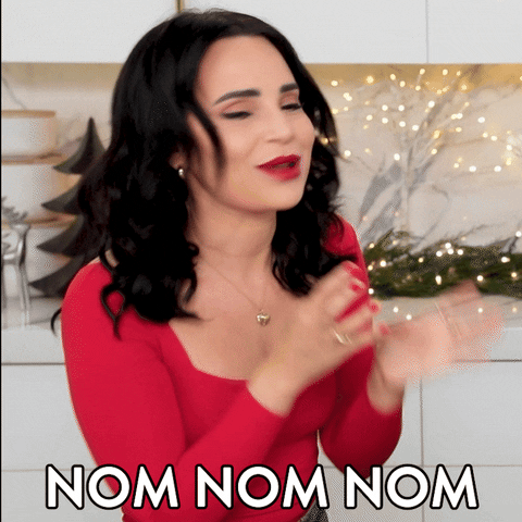Celebrity gif. YouTuber Rosanna Pansino, wearing a bright red shirt with matching red nail polish and lipstick, smacks her lips together and wiggles her fingers near her mouth in anticipation. Text reads, "Nom nom nom."