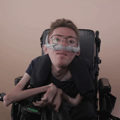 Reaction gif. A mobility-impaired white man using a power chair, a ventilator, and wearing retro-crossbar glasses rolls his eyes at you.