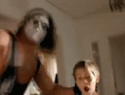 Video gif. Young boy and wrestler Sting are in a normal suburban home. They bang their heads on the wooden railing of a staircase, the boy stumbles backwards. Sting picks up the boy and makes him bulldoze the different stuff on top of a fireplace mantle. Sting then throw the boy into a china cabinet while the parents watch.