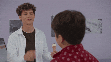 Video gif. Teen boy holds an ice cream cone in one hand and high fives another boy, smiling.