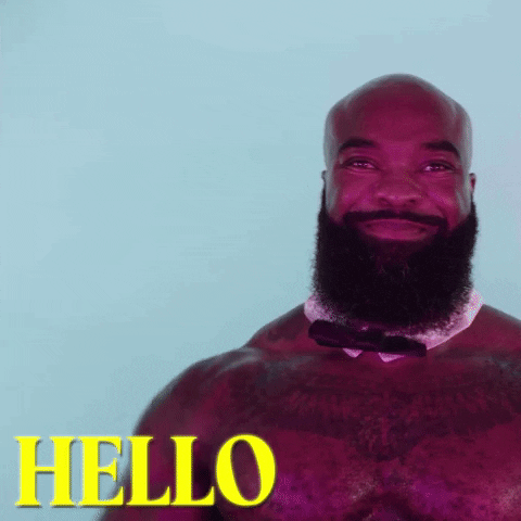 Video gif. Hunky shirtless muscular man with a hairy chest, big beard, and star-shaped tattoo waves at us with a smile as he enthusiastically says “Hello.”