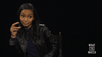 Celebrity gif. Yara Shahidi leans on the arm of a director's chair, giving a side eye and snapping her fingers.