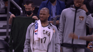 Sports gif. PJ Tucker stands on the sidelines of a Bucks game. He looks at the court, squinting his eyes in confusion, and tilts his head side to side as he tries to figure out what’s happening.