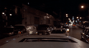 Movie gif. Tom Hanks as adult Josh in Big wears a white tux and holds his arms up as he emerges through the sunroof of a moving car, then looks around in awe.  