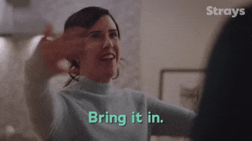 TV gif. Nicole Power as Shannon Ross has a wide smile on her face, holding her arms out and waving her hands to beckon someone over for a hug as she says, “Bring it in.”
