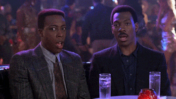 Movie gif. Eddie Murphy as Prince Akeem and Arsenio Hall as Semmi sit in a nightclub staring at something with shock and open mouths.