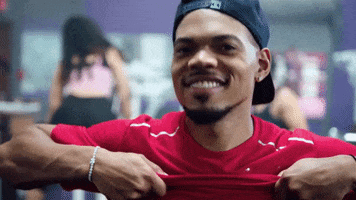 Music video gif. Chance the Rapper is in a gym and is pulling his shirt up. He has a broad, pleased grin on his face as he nods in satisfaction.