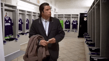 Sports gif. John Travolta as Vincent in Pulp Fiction superimposed into an empty footballer locker room, looks around and shrugs in wonder.