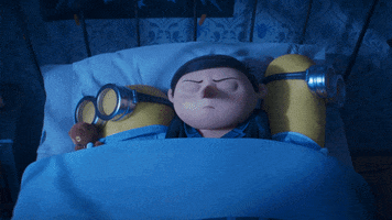 Despicable Me gif. A young Gru and two Minions lay asleep in bed. A cheery third Minion in a red bathrobe leaps into bed, waking them up as he makes himself comfortable. Gru is annoyed, but the Minion with the teddy bear doesn't seem bothered in the least.