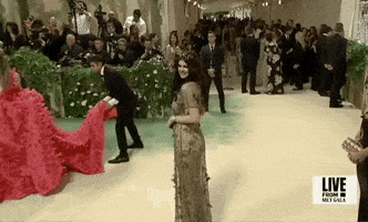 Met Gala 2024 gif. Alexandra Daddario poses for the cameras, one way, then the other, wearing an edgy golden Dior Haute Couture gown.