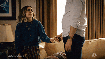 TV gif. Mae Whitman as Annie Marks in Good Girls stands up from her couch and pulls Rob Heaps as Dr. Josh Cohen into a sweet hug.