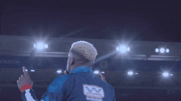 Sports gif. Cedric Kipre walks in slow-motion, with his back to us, down a soccer field in his Wigan gear with his elbows at his sides and his index finger pointing up.