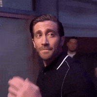 Celebrity gif. With a bittersweet look, Jake Gyllenhaal touches his fingers to his lips, closes his hand into a fist, and walks away, disappearing into a room full of smoke.