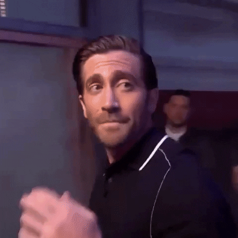 Celebrity gif. With a bittersweet look, Jake Gyllenhaal touches his fingers to his lips, closes his hand into a fist, and walks away, disappearing into a room full of smoke.