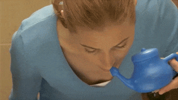 Video gif. A woman holds a neti pot up to her nostril and tilts her head. Water pours out the other nostril. 