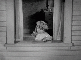 Movie gif. A toddler on Our Gang carelessly tosses a handful of money out an open window. 