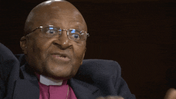 Video gif. Archbishop Desmond Tutu flashes excited eyes and seems to say "Oh" during an interview.