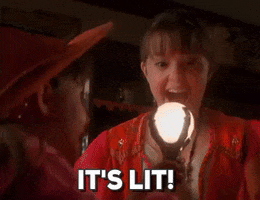 Disney gif. Emily Roeske, as Sophie in Halloweentown, hands a glowing orb to Kimberly J. Brown, as Marnie, who receives it with surprised delight. Text, "It's lit!"
