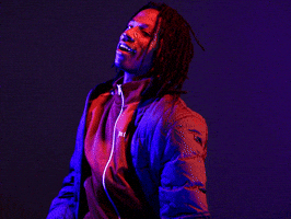 Celebrity gif. Joey Badass wears an unzipped puffer jacket with a cool smile, lit by red and blue lights and shimmying his shoulders.