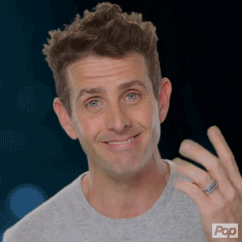 Reality TV gif. Joey McIntyre, on Rock This Boat: New Kids on the Block, smiles a toothy grin at us and points to his dimples with his fingers.