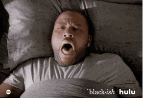 TV gif. Andy Anderson as Dre Johnson on Black-ish lays in bed and yawns widely, covering his mouth with a fist.