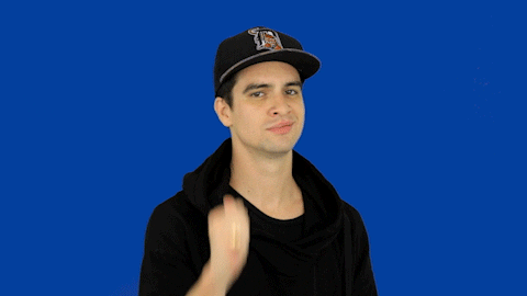 Video gif. Against a solid blue background, Brendon Urie of Panic! at the Disco gives us a thumbs up, a nod, and an understated smile.