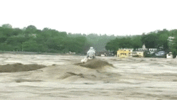 Video gif. White statue of Krishna surrounded by brown floodwaters up to the statue's neck remains unmoved and parts the water around it as it is drug through the water.