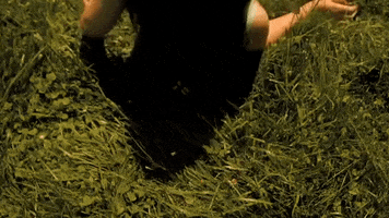 Video gif. From above, we see a tired girl lying down on the grass.