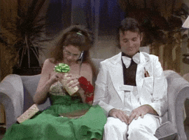 SNL gif. Sitting on a couch, dressed up for a school dance, Gilda Radner as Lisa opens up a can that explodes with a prank snake and she screams, while Bill Murray as Todd laughs awkwardly next to her.