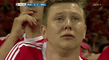 Video gif. A player from the russian national football team exhales sharply as tears fill his eyes and he bows his head to wipe his eyes. 