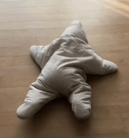 Video gif. A baby in a puffy starfish costume struggles to wiggle across the floor. 