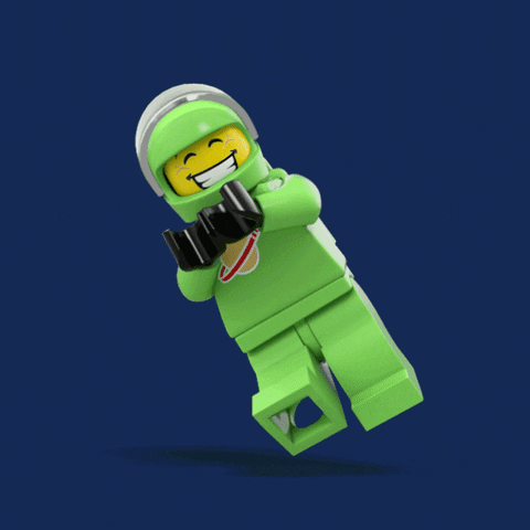 Digital art gif. Green astronaut lego man floats in the air, kicking his legs and clapping excitedly. His helmet shield is up, revealing a huge grin on his face.