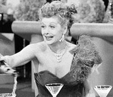 TV gif. Lucille Ball from I Love Lucy dressed in a fancy gown and flashy jewelry, excitedly and haphazardly pouring champagne over glasses and the table.