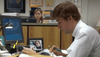 The Office gif. John Krasinski as Jim sits at his desk typing slowly. We can see Jenna Fischer as Pam at her desk in the background. Jim slowly gives up, planting his face on his desk, and Pam smiles in reaction in the background.