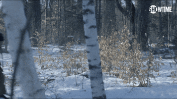 TV gif. Michael C. Hall as Dexter Morgan in Dexter runs through a snowy forest with a rifle under his arm. He appears panicked and afraid.