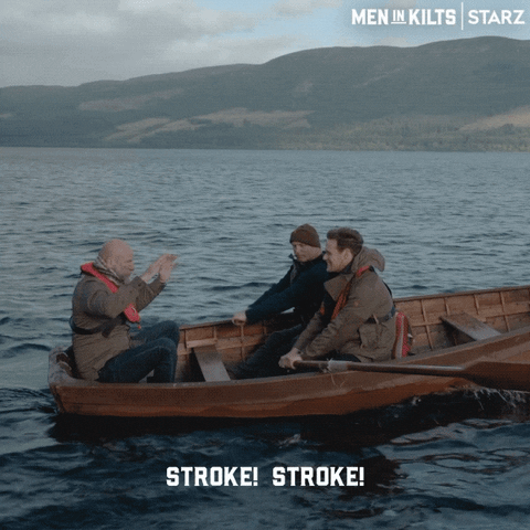 TV gif. Hosts Sam Heughan and Graham McTavish of Men in Kilts row across loch ness with Outlander actor Gary Lewis. Text, "Stroke! Stroke!"