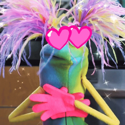 Video gif. Green puppet with hearts for eyes and fluffy neon eyelashes presses its pink hands to its chest, overcome with love.